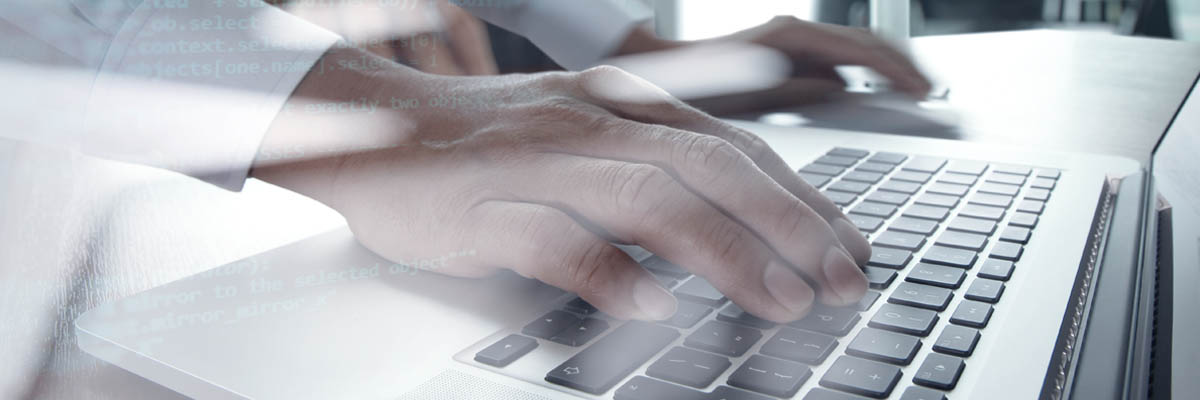 A person typing on a laptop with computer code in the foreground.